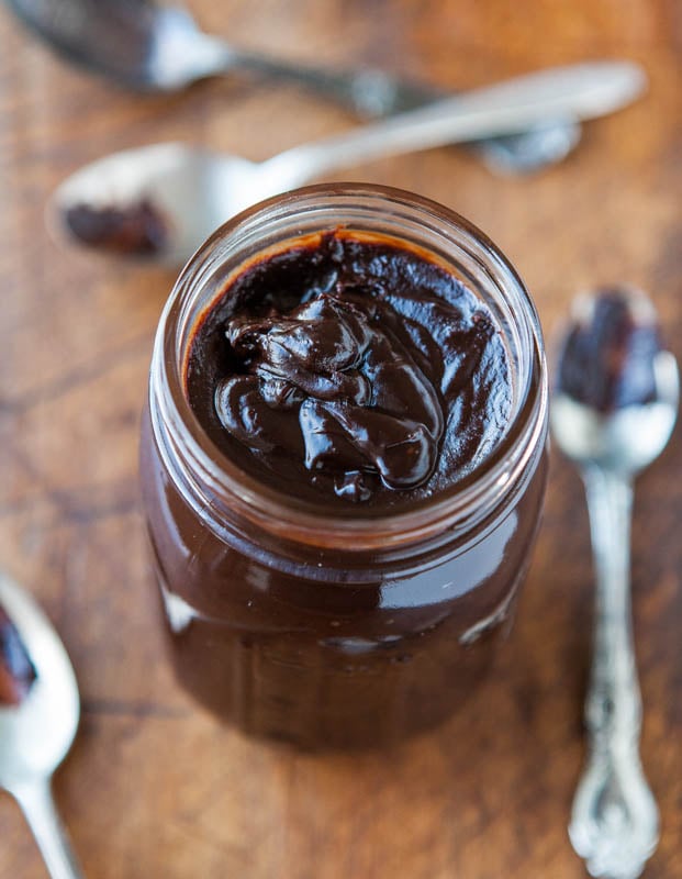 homemade hot fudge in glass jar surrounded by spoons