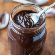 A jar of homemade hot fudge with a spoon sticking out.