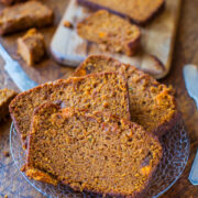 Slices of homemade pumpkin bread on a plate with more pieces on a wooden cutting board in the background.