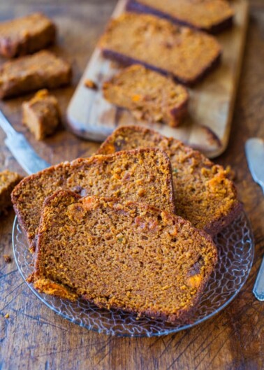 Slices of homemade pumpkin bread on a plate with more pieces on a wooden cutting board in the background.