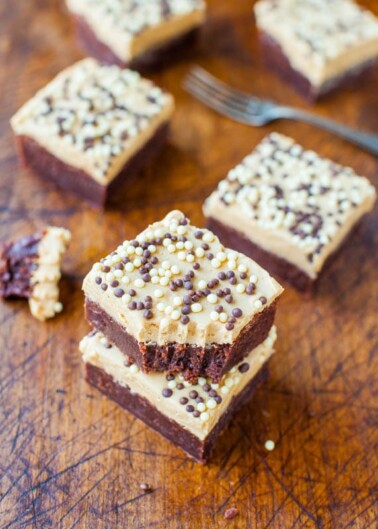 Homemade chocolate brownies topped with a layer of peanut butter and decorated with assorted sprinkles, displayed on a wooden surface.