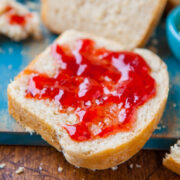 A slice of bread with strawberry jam on a wooden board.