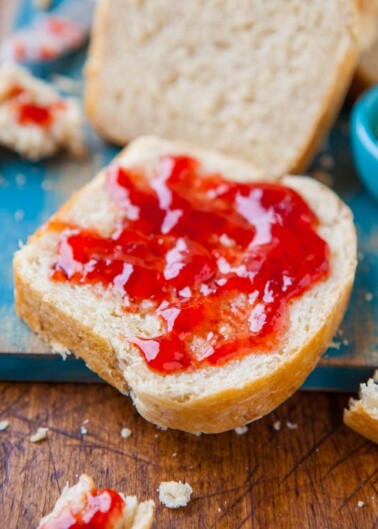 A slice of bread with strawberry jam on a wooden board.