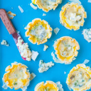 Mini blue cheese tartlets on a blue background with a cheese spreader.