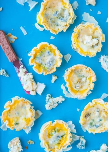 Mini blue cheese tartlets on a blue background with a cheese spreader.