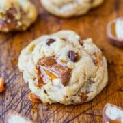 Freshly baked chocolate chip cookie with caramel pieces on a wooden surface.
