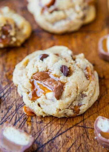 Freshly baked chocolate chip cookie with caramel pieces on a wooden surface.