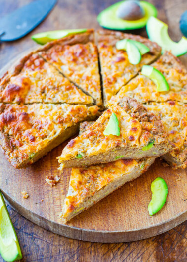 A freshly baked quiche with avocado slices on a wooden cutting board.