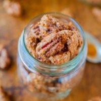 A jar filled with candied pecans on a wooden surface.