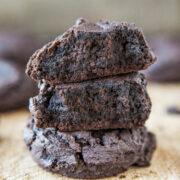 Three chocolate cookies stacked on a wooden surface.
