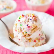 Scoop of colorful sprinkle-dotted ice cream on a spoon, with more in a bowl in the background.