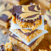 Stack of homemade peanut butter bars with chocolate topping on a wooden surface.