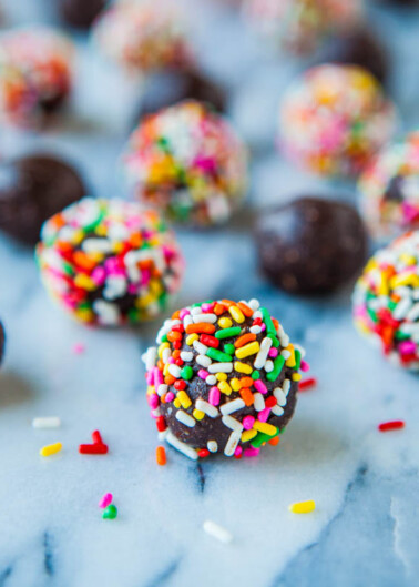 Colorful sprinkles covering chocolate truffles on a marble surface.