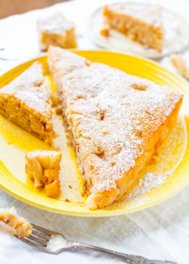 Slices of apple cake dusted with powdered sugar on a yellow plate.