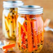 A jar of pickled carrots with spices on a wooden surface.