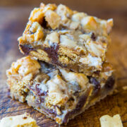 Stacked homemade dessert bars with chocolate chips and nuts on a wooden surface.