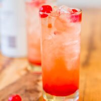 A refreshing glass of iced red cocktail garnished with cherries on a wooden surface.