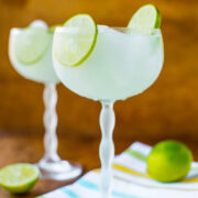 Two glasses of margarita with lime garnishes on a wooden surface.