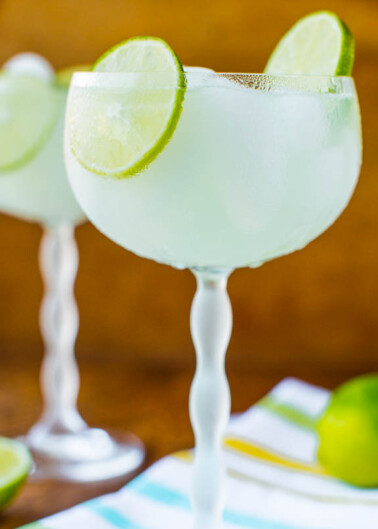 Two glasses of margarita with lime garnishes on a wooden surface.