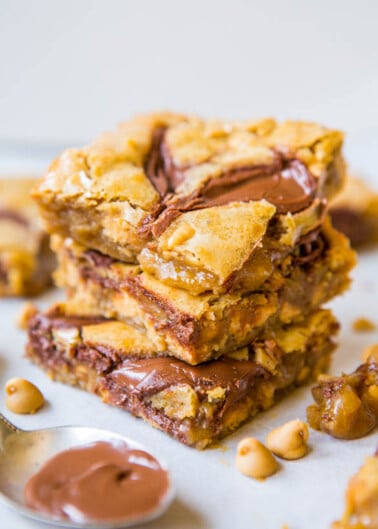 A stack of peanut butter blondies with chocolate swirls and whole peanuts on a plate.