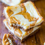 A close-up of a creamy swirled cheesecake bar with chunks of caramel on a wooden surface.