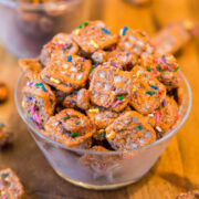 A plastic cup filled with colorful, sprinkled, frosted cereal treats on a wooden surface.
