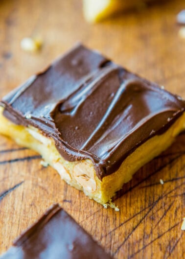 A close-up of a chocolate caramel shortbread square on a wooden surface.