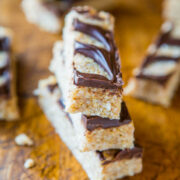 Stacked cereal bars with chocolate drizzle on a wooden surface.