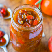 Jar of homemade tomato relish with fresh tomatoes in the background.