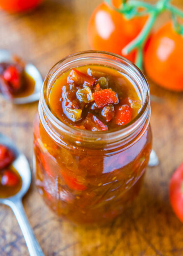Jar of homemade tomato relish with fresh tomatoes in the background.