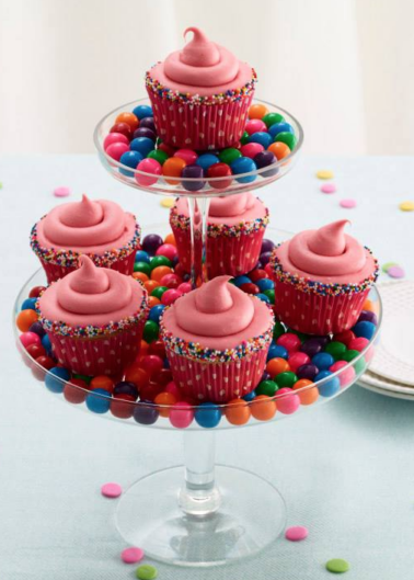 Three-tiered dessert stand displaying pink frosted cupcakes and multicolored candies.