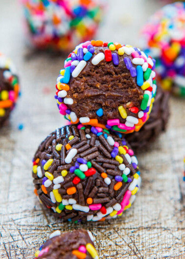 Colorful sprinkle-covered chocolate truffles on a wooden surface.