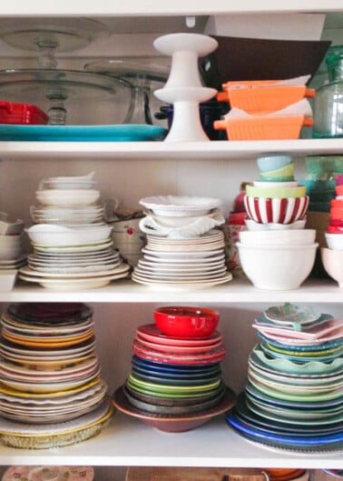 An organized kitchen cabinet with neatly stacked plates and bowls in various colors and sizes.