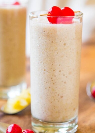 Two glasses of creamy milkshakes garnished with red cherries on a wooden table.