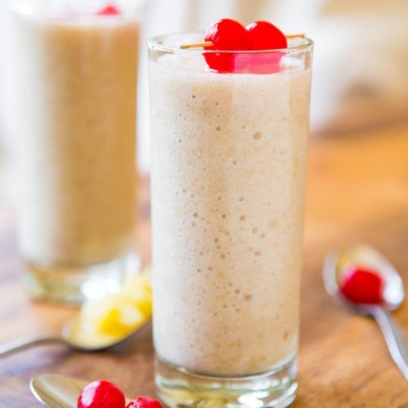 Two glasses of creamy milkshakes garnished with red cherries on a wooden table.