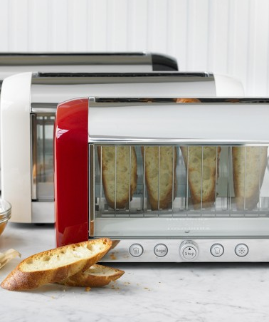 A modern red toaster oven toasting slices of bread on a kitchen counter, with a traditional toaster in the background.