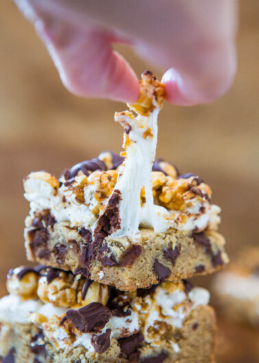 A hand pulling a piece of a gooey, marshmallow-caramel popcorn bar with chocolate chunks.