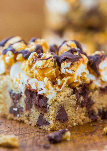 A close-up of a dessert bar with a cookie base, chocolate chunks, marshmallows, and drizzled chocolate topping.