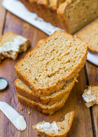 Slices of freshly baked bread with one topped with cream cheese, and a butter knife on the side.