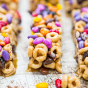 Rows of homemade cereal bars with chocolate chips and colorful candies on a wooden surface.