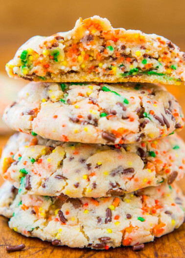 A stack of colorful sprinkle cookies with one cookie on top bitten in half.