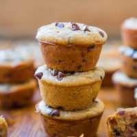 A stack of three chocolate chip muffins on a wooden surface.