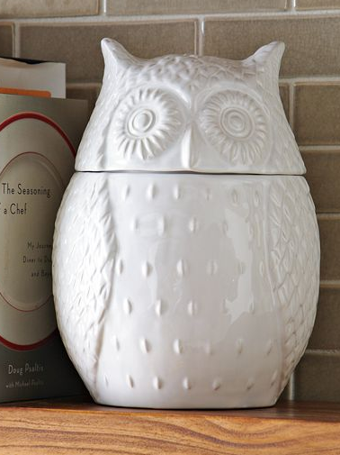 A ceramic owl-shaped kitchen utensil holder on a countertop next to cookbooks.