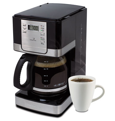 Programmable coffee maker with a digital clock display, brewing coffee into a carafe next to a filled coffee cup.