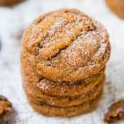 A stack of sugar-coated ginger cookies on a wooden surface with a spoonful of syrup nearby.
