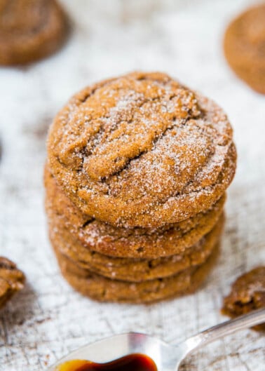A stack of sugar-coated ginger cookies on a wooden surface with a spoonful of syrup nearby.