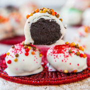 Chocolate truffles with white coating and sprinkles on a red mat.
