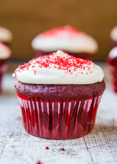 A red velvet cupcake with cream cheese frosting and red sprinkles on top.