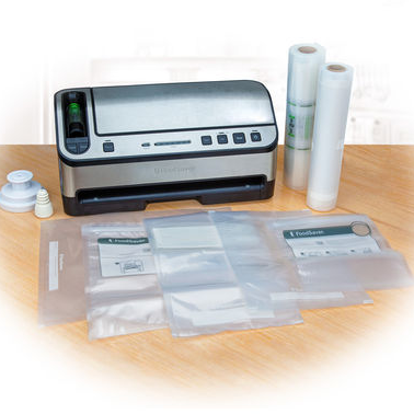 Vacuum sealer with rolls of sealing bags and assorted sealed items on a table.
