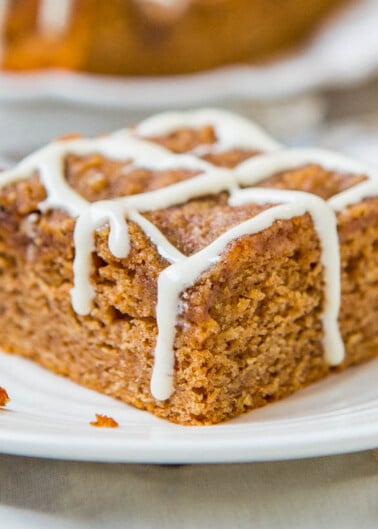 A slice of carrot cake with white icing drizzle on a white plate.